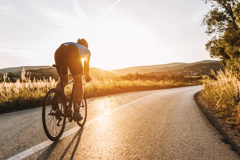 Rennradfahrer fährt auf einer Landstraße der Sonne entgegen